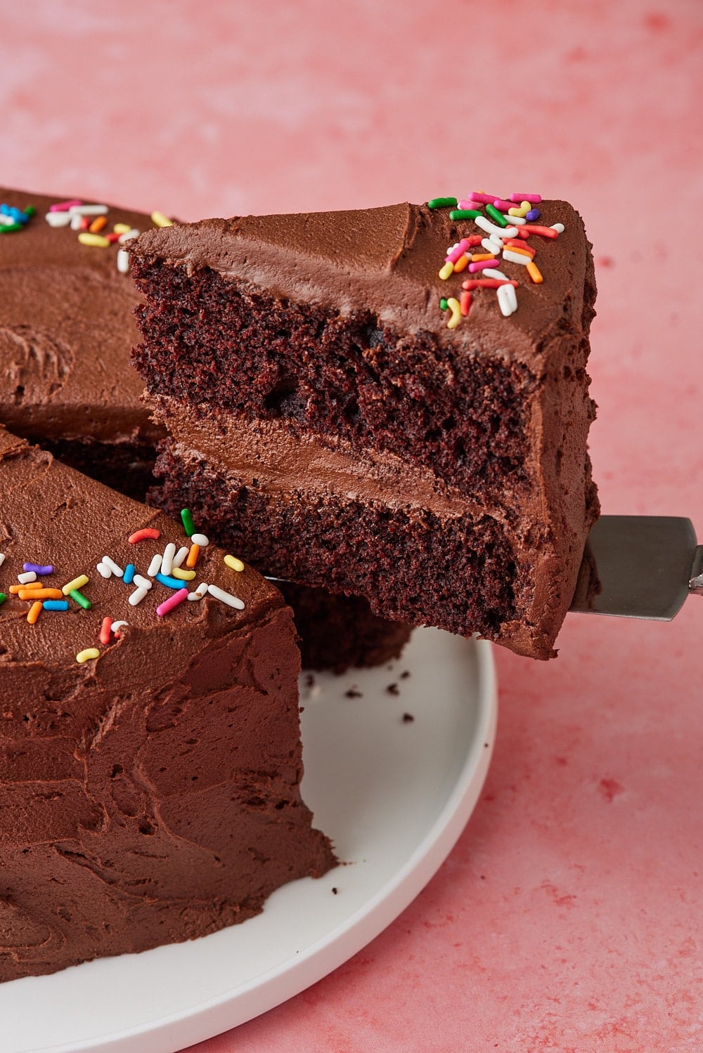 A close-up shot at a slice of chocolate cake shows its moist crumb and rich chocolate buttercream frosting. 