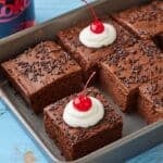 Coca Cola Cake squares in a baking tray, with moist crumb, rich frosting, whipped cream and cherries.