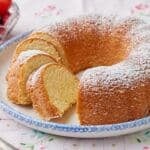 A Hot Milk Cake is dusted with powdered sugar and partially sliced, served with fresh berries on the side.