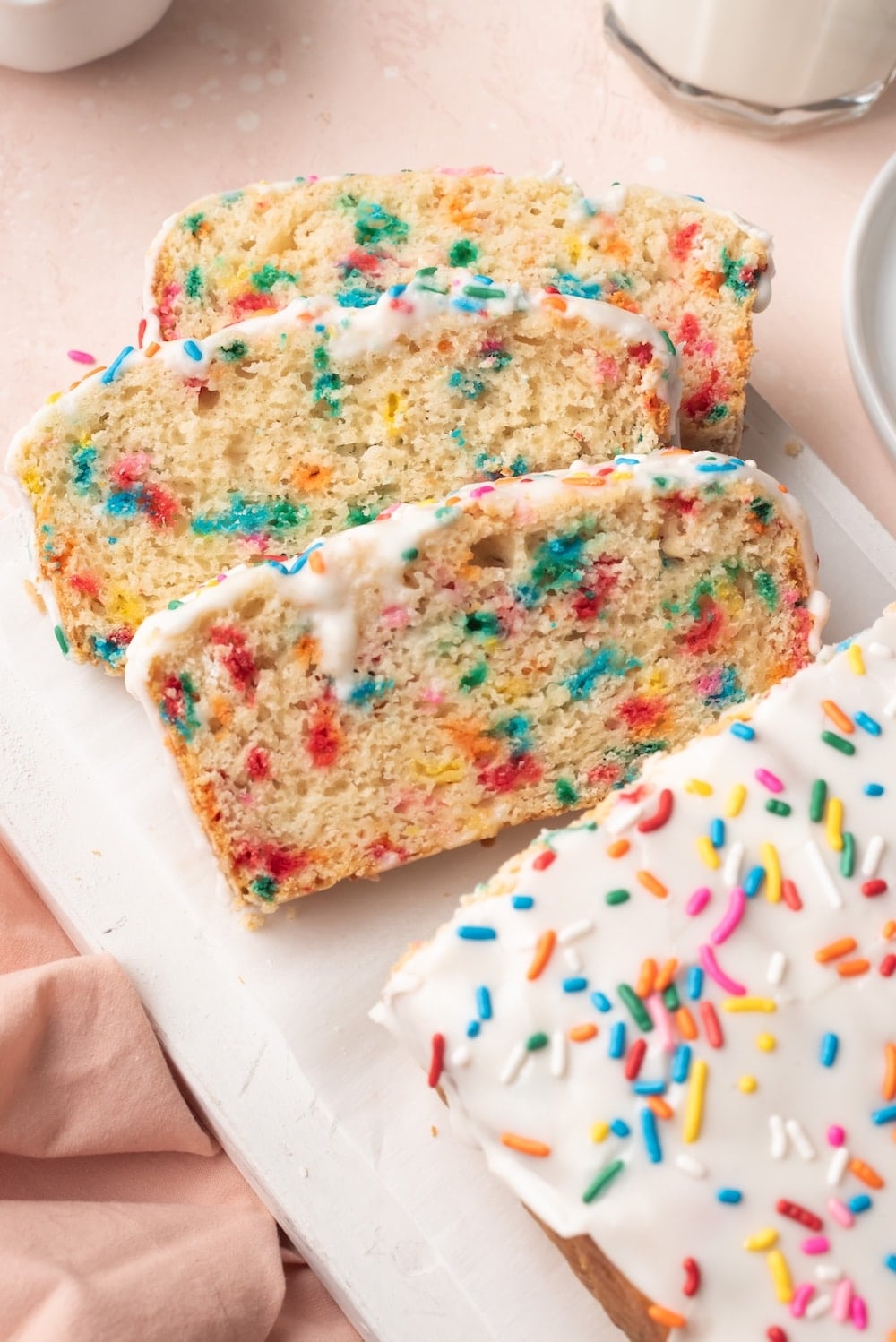 Ice Cream Bread with half loaf sliced into three slices. It's covered with icing and has sprinkle in the crumb and icing.