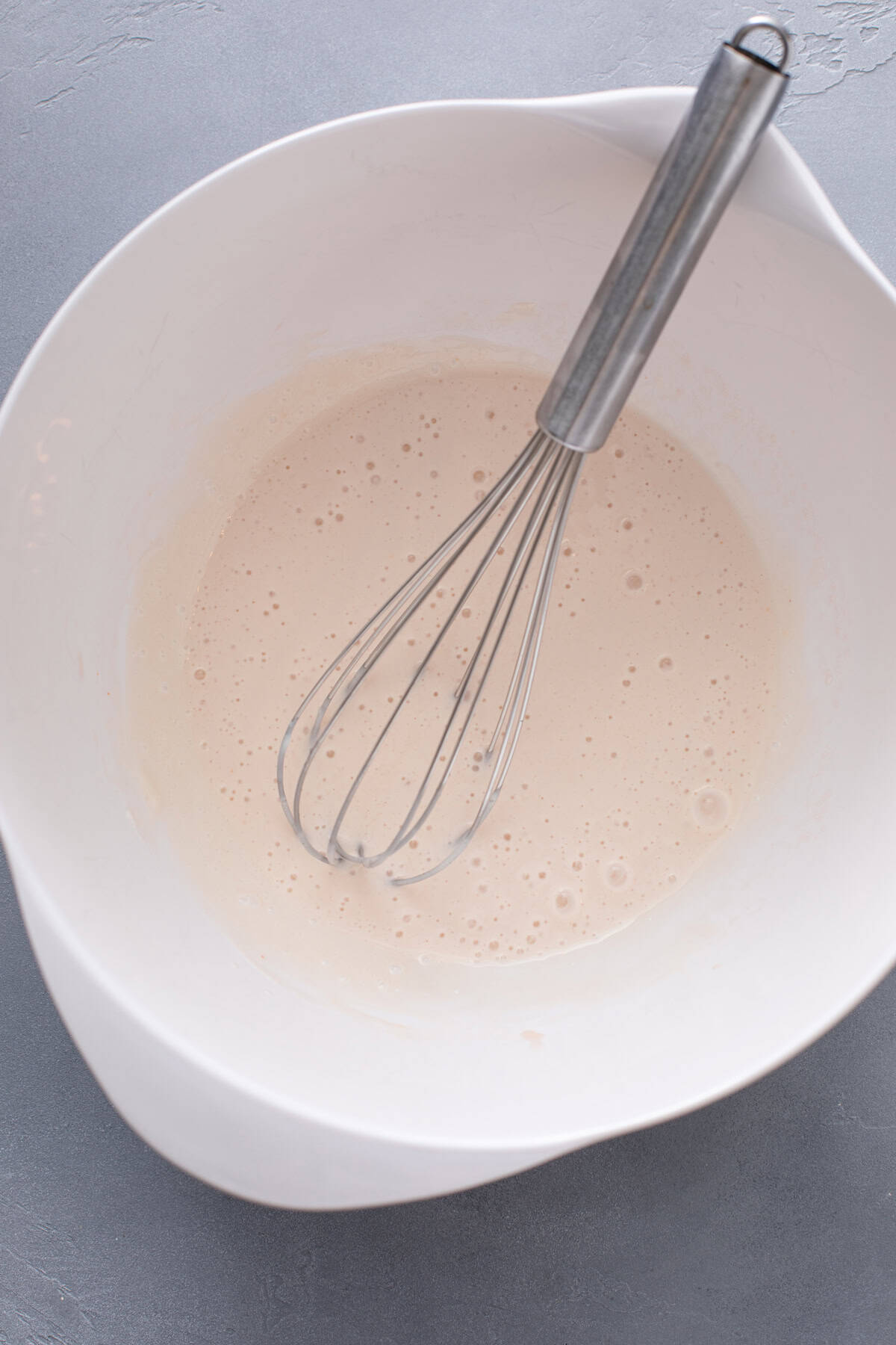 Dressing for broccoli salad being whisked in a white bowl.