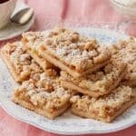 A plate of Apple Crumble Bars dusted with powdered sugar, served with coffee on the side.