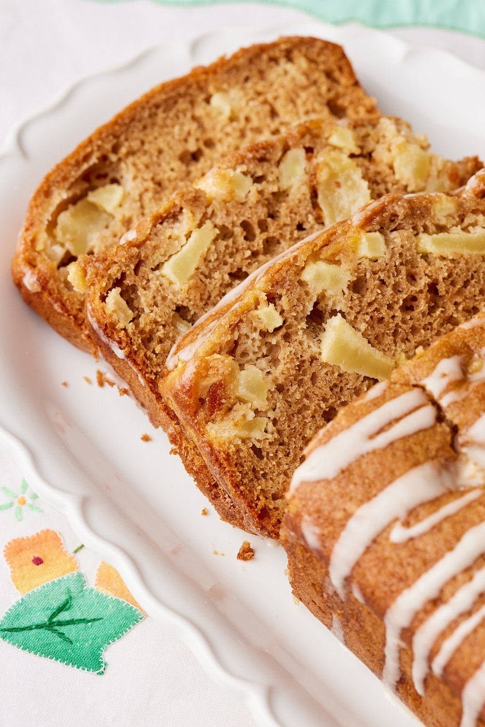 Slices of moist Apple Loaf Cake packed with diced apples and warm cinnamon, topped with a simple apple glaze on a white platter.