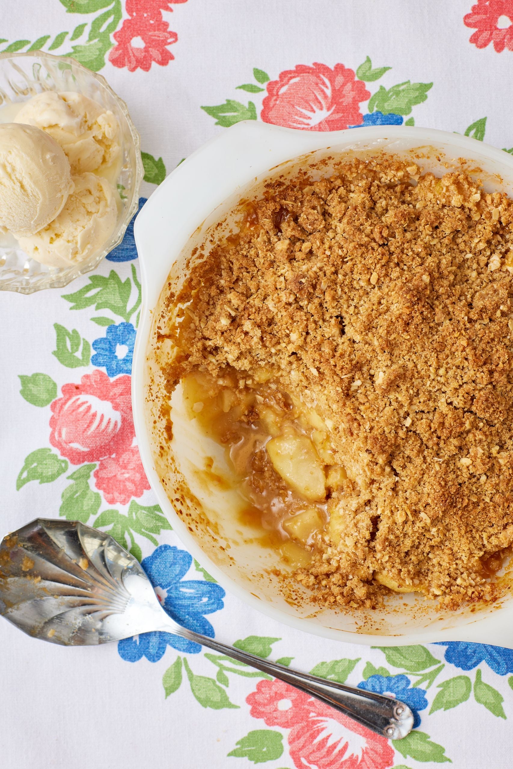 A bowl of apple crisp with a scoop taken, ice cream is served on the side.