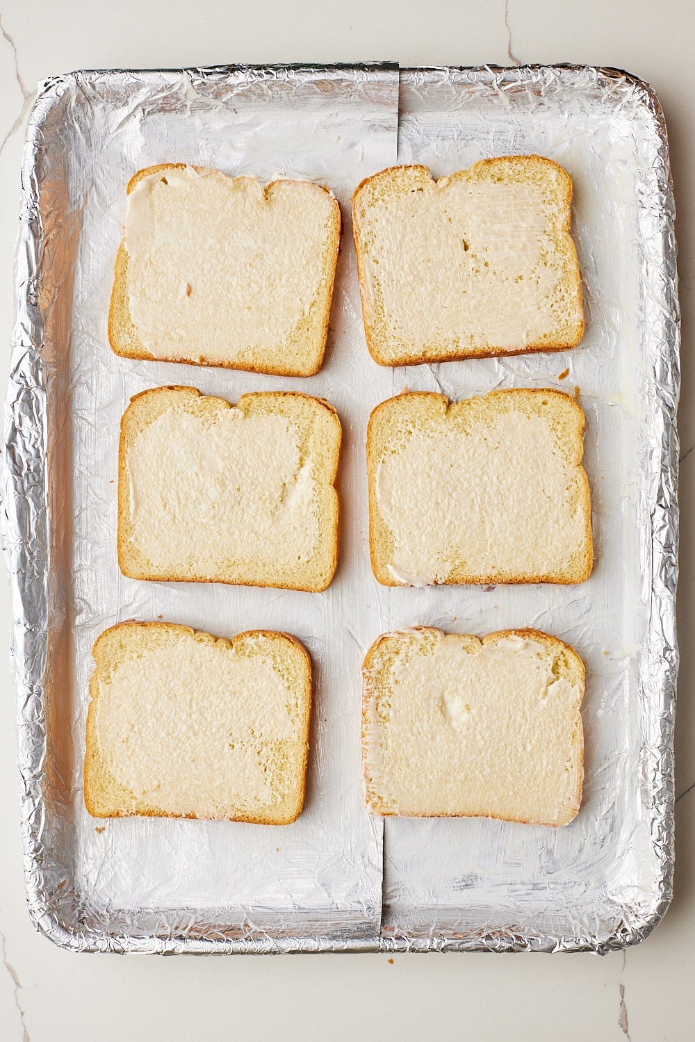 Buttered brioche slices arranged on a foil-lined sheet pan, ready to make Sheet Pan French Toast. 