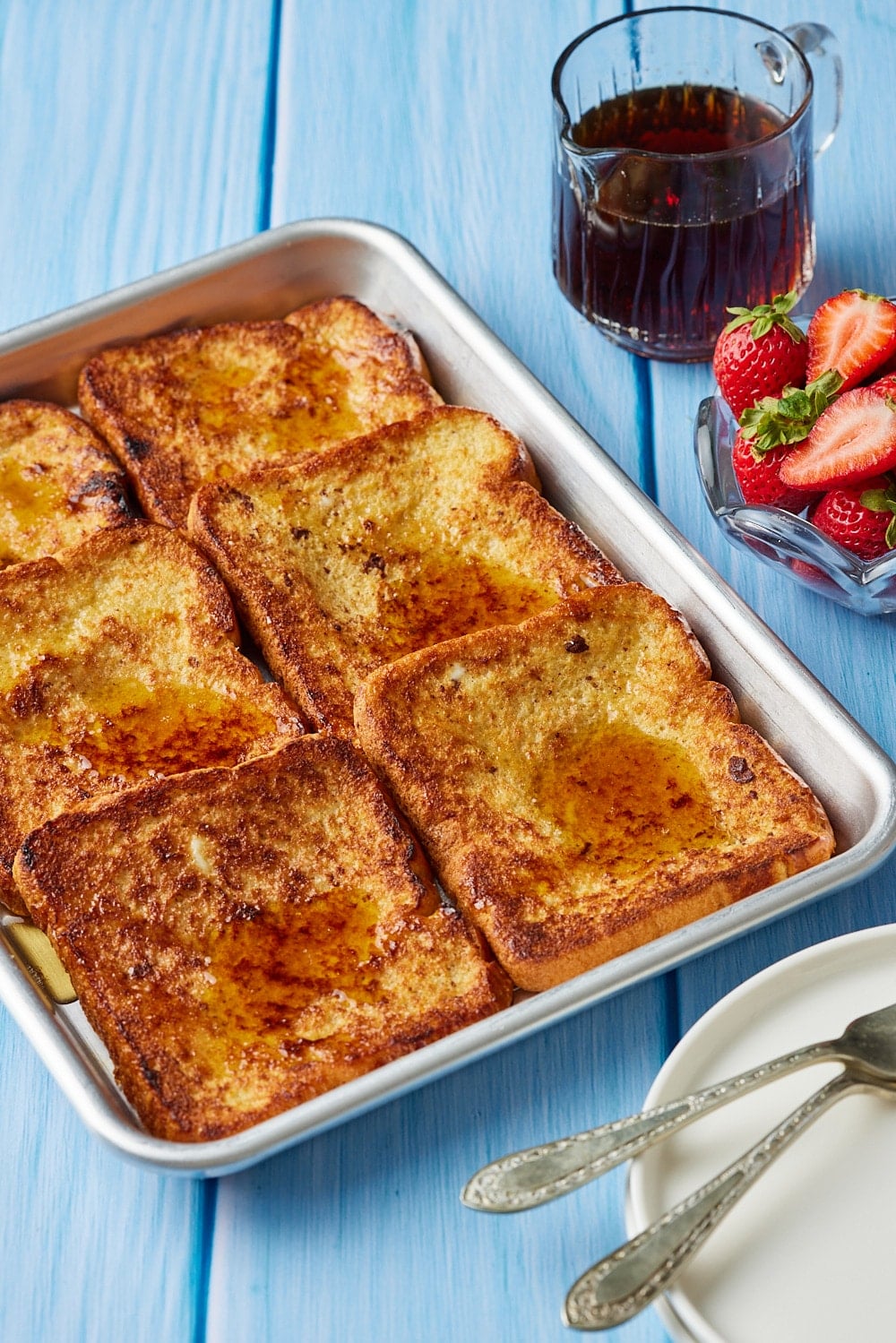 Sheet Pan French Toast served with maple syrup and fresh strawberries.